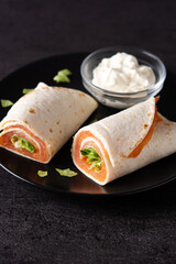 Salmon wrap sandwich roll with cheese and vegetables on black background