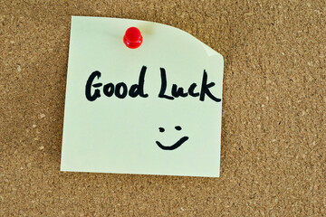 Yellow sticky note with good luck wishes on cork board
