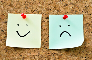 Sticky notes sad and happy face expression on cork board