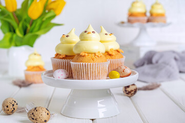 Cute Easter chick cupcakes. Vanilla cupcakes with buttercream on a white stand with fresh flowers on a white wooden background. Copy space.
