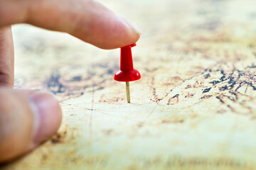 Hand holding red pushpin on map