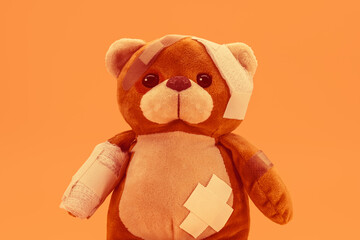 Teddy bear toy with bandages and bandages, image in orange tone for the month of MAY ORANGE, about preventing child abuse and violence against children