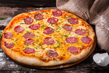 pizza with cheese sausage salami and herbs on a wooden board 