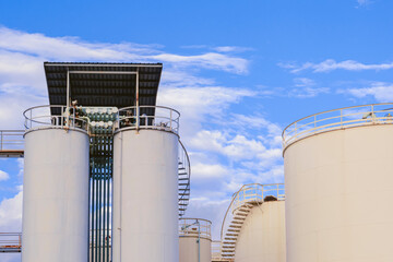 Storage fuel tanks with silos and pipeline system against clouds on blue sky in chemical and petroleum industrial area