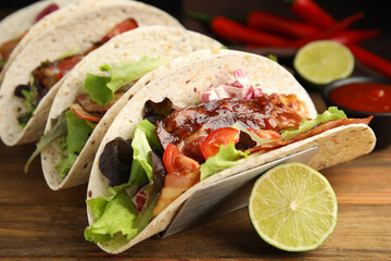 Delicious tacos with fried bacon and lime on wooden table, closeup