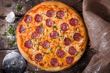pizza with cheese sausage salami and herbs on a wooden board 