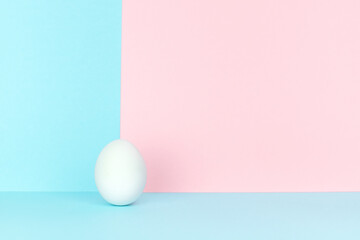 Single white egg on crossing point of blue and pink backgrounds. Easter concept.