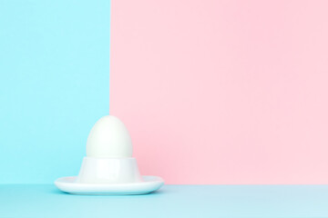 Single white egg on crossing point of blue and pink backgrounds. Easter concept.