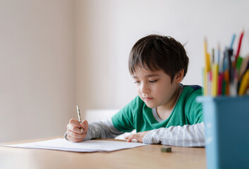 Happy boy using pencil drawing or sketching on paper, Portrait  kid siting on table doing homework, Child enjoy art and craft activity at home, Education concept