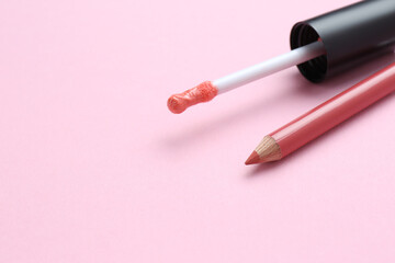 Lip pencil and brush of liquid lipstick on pink background, space for text. Cosmetic products