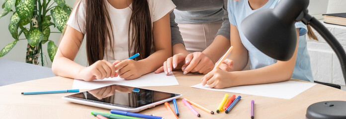 Beautiful young mother helping her daughters with homework.