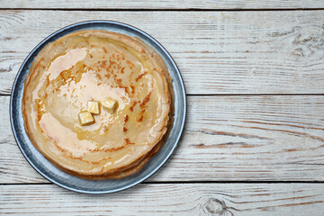 Delicious crepes with melting butter on white wooden table, top view. Space for text