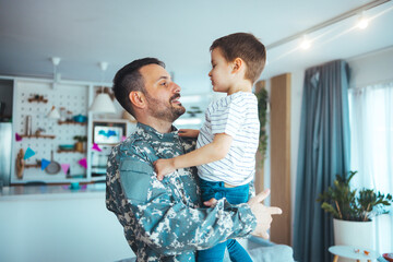 Playful military man having fun with his small son at home. A military dad and his son are hugging in their living room. The son is smiling happily