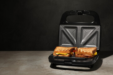 Modern grill maker with tasty sandwiches on light grey table. Space for text