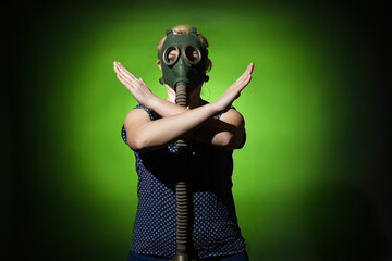 blonde woman in a gas mask shows a stop signal with crossed arms on a dark dramatic background,...