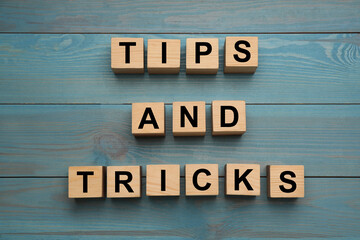 Phrase Tips and Tricks made with wooden cubes on light blue table, flat lay