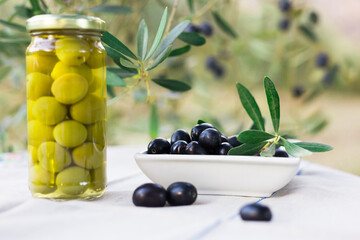 canned olives in a glass jar, oil and olives on the table against the background of the olive garden