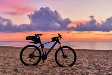 Bicycle on sandy sea coast against backdrop of pink idyllic sunset. Active vacation time