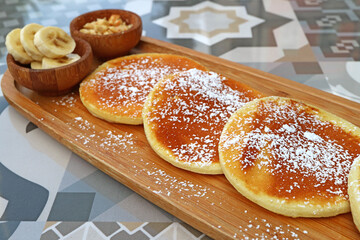 Pancakes with icing sugar on wooden plate served on patterned stone table
