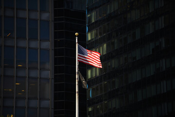 The national flag of the United States of America waving in dramatic sun light between the tall skyscrapers in Manhattan, New York.