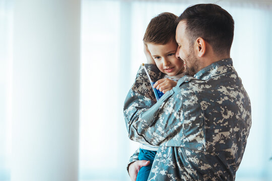 Happy military man with his son at home. An emotional military father, dressed in camouflage, holds his young son in arms in greeting after returning home from a tour of duty overseas.