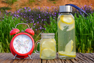 Freshness concept. Lemonade with alarm clock and lemon slices in a jar on a rustic  wooden background. Close up.