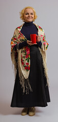 woman holding a red cup in her hands in traditional colored Russian headscarf on a white background