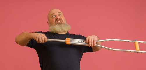 angry man in a black t-shirt breaks a crutch on a pink background