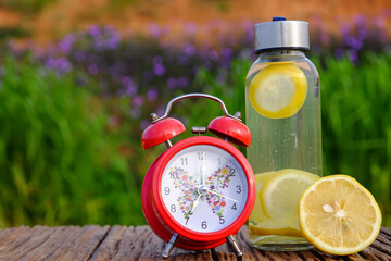 Freshness concept. Lemonade with alarm clock and lemon slices in a jar on a rustic  wooden background. Close up.