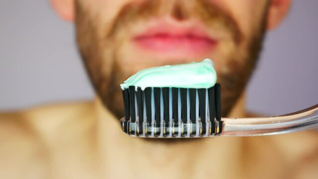 Close-up of a black toothbrush and a young man squeezes toothpaste onto it