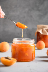 Homemade apricot jam or marmalade in spoon on gray kitchen tabletop. Seasonal canned food. Close up. Vertical format.