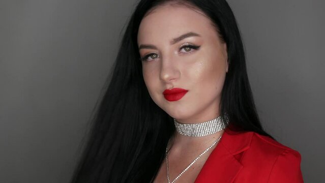 Beautiful girl model with big lips painted with red lipstick. Young woman posing in stylish red Blazer necklaces made of rhinestones and bright evening make-up, looking at the camera