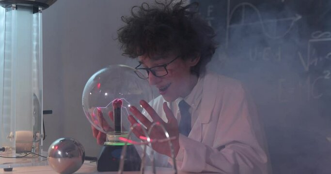 Education, science and kids concept - boy wearing goggles for physics lab doing electrical tests. Child studying electrical discharges in a lab.