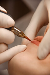 beauty procedure. close up permanent lip tattoo. master in white medical gloves makes permanent lip...