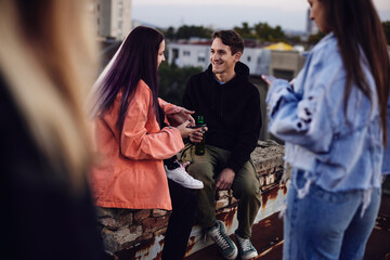 Three teenage friends sitting on the rooftop, chilling and drinking beer.
