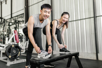 Obraz premium exercise concept The man and woman in the sport club resting one of their feet on the black bench and trying to tie up their shoelace