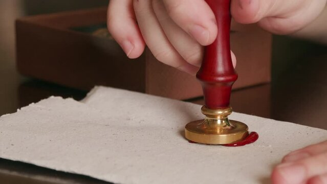 Pressing a wax seal into hot wax on a piece of parchment, sealing the letter.