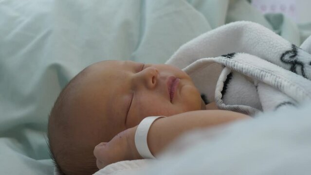 Newborn Caucasian baby with wristband asleep under blanket
