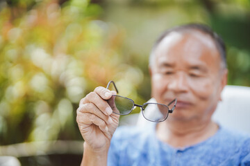 Elderly man holding eyeglasses in hand and looking at glasses, selective focus.