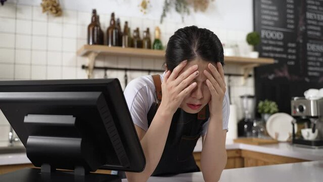 closeup stressed Chinese coffee shop owner is bending over the counter and propping face worrying about business after checking order on the cashier machine.