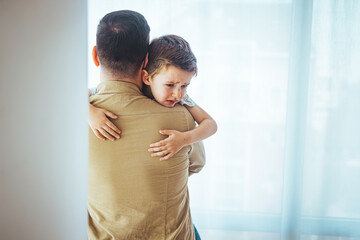 Closeup Sad young blond boy crying on father hands indoor. Man holds son, hugs and comforts. Family...