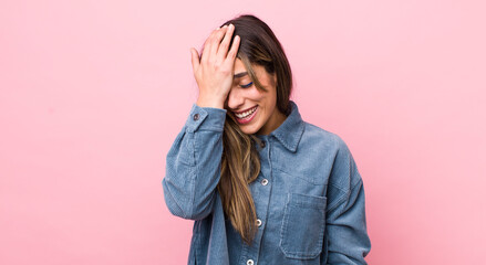 pretty hispanic woman laughing and slapping forehead like saying d’oh! I forgot or that was a...