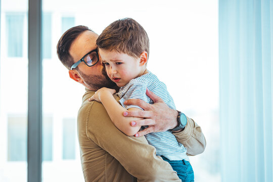 Closeup Sad young blond boy crying on father hands indoor. Man holds son, hugs and comforts. Family love, care and moral support, baby's tears, daddy's arms. Dad consoling crying child