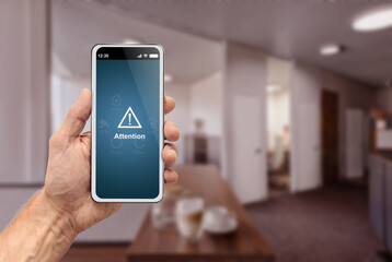 Male hand holding modern smartphone with security alarm app on screen over office background