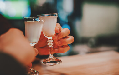 Two hands clinking shots of alcoholic beverage in bar
