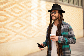 Handsome guy drinking coffee while walking in the street. Modern fashion man using the phone