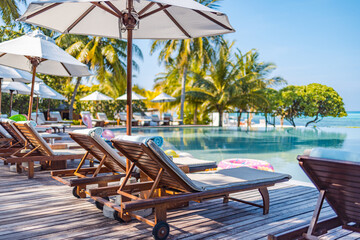 Umbrellas and chairs around outdoor swimming pool in resort hotel for vacation leisure lifestyle. Luxury destination concept, lounge closeup scenic under palm trees, relax, tranquil vibes