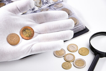 Collection of coins and collector white gloves and magnifying glass on white