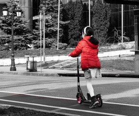 A little girl, dressed in a red winter jacket, walks on a scooter, kickboard.
