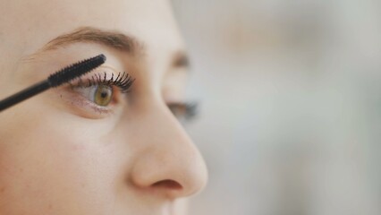 Fototapeta premium Make-up on the face. Close-up of a young woman painting her long eyelashes with black mascara.